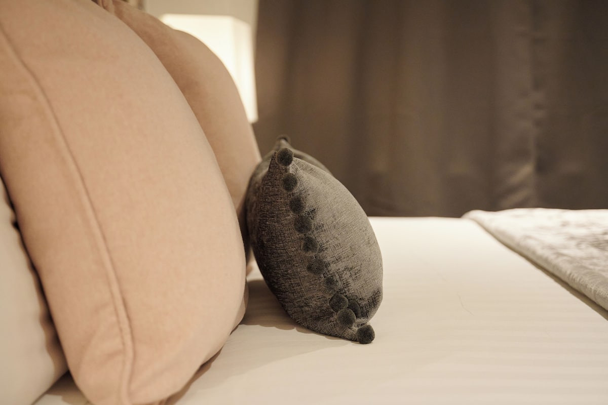 A bed with two pillows, one beige and one gray with pom-poms.