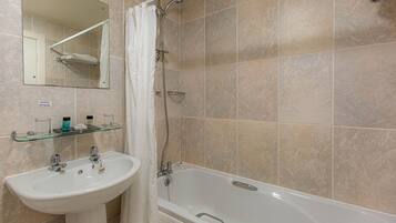 A bathroom with a sink, mirror, shower, and tiled walls.