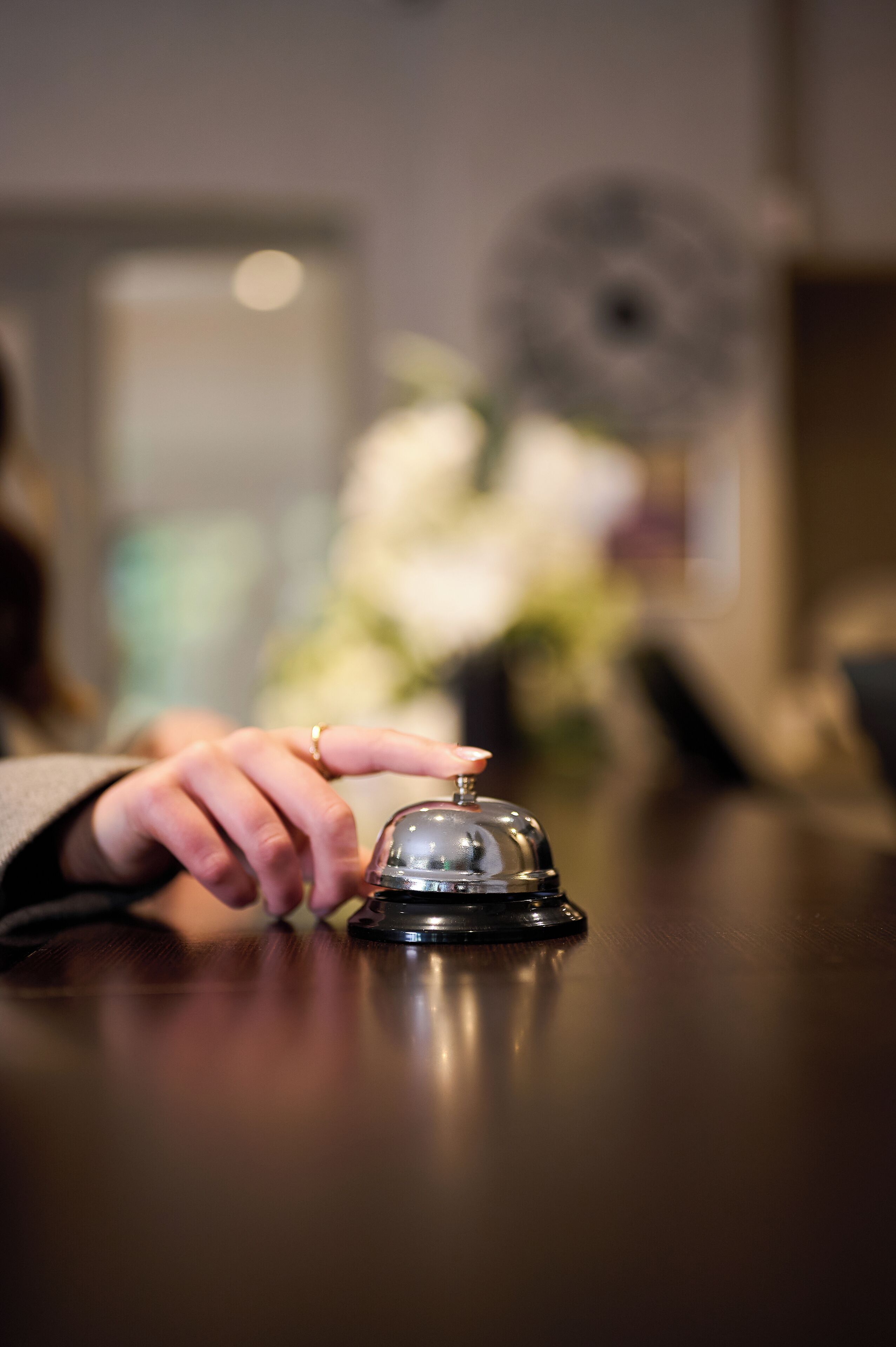 A hand pressing a hotel room's bell, with a blurred background suggesting indoor setting.