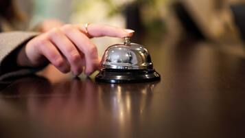 A hand pressing a hotel room's bell, with a blurred background suggesting indoor setting.