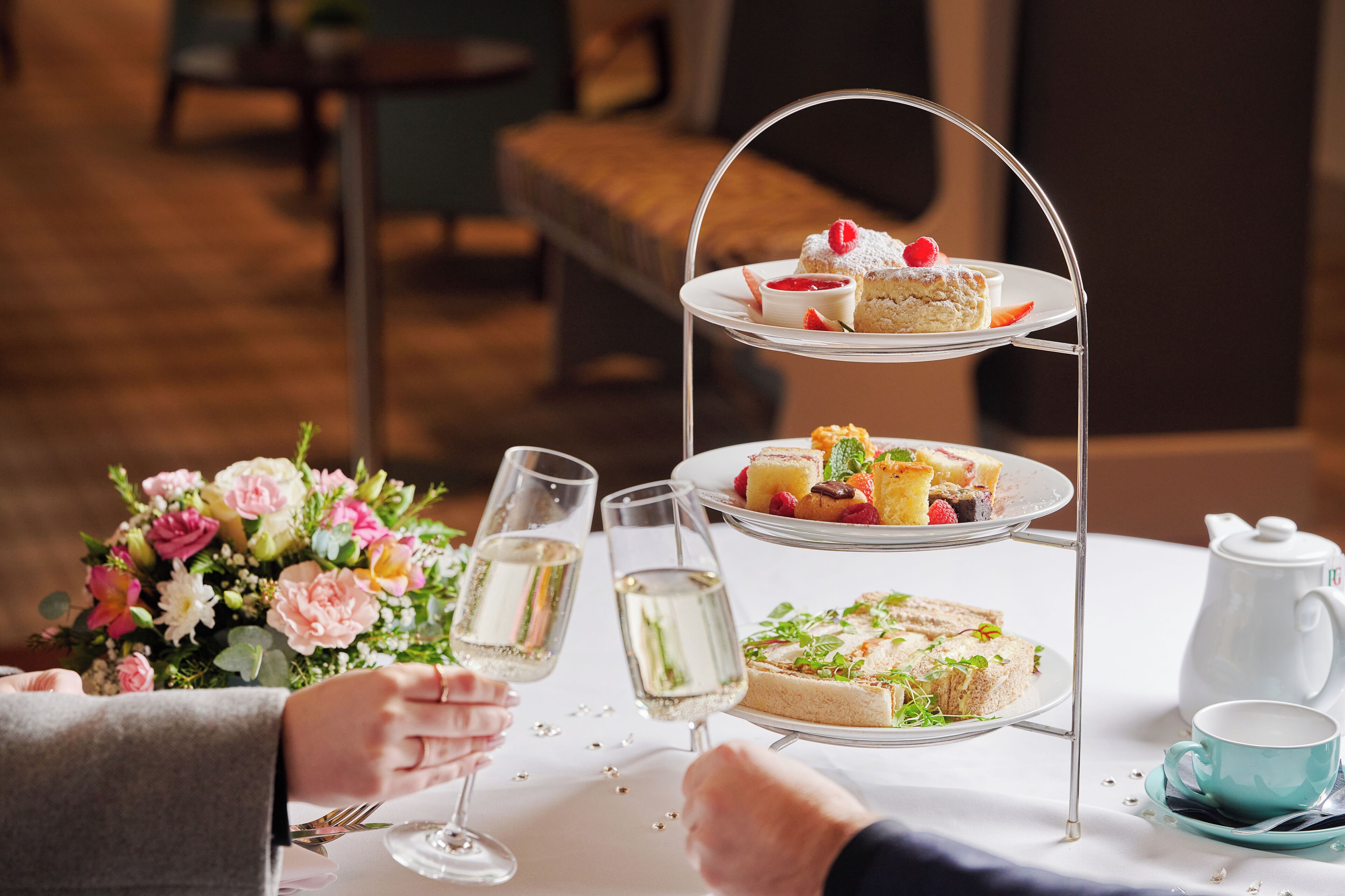 A three-tiered dessert stand with various pastries and a teapot on a table.