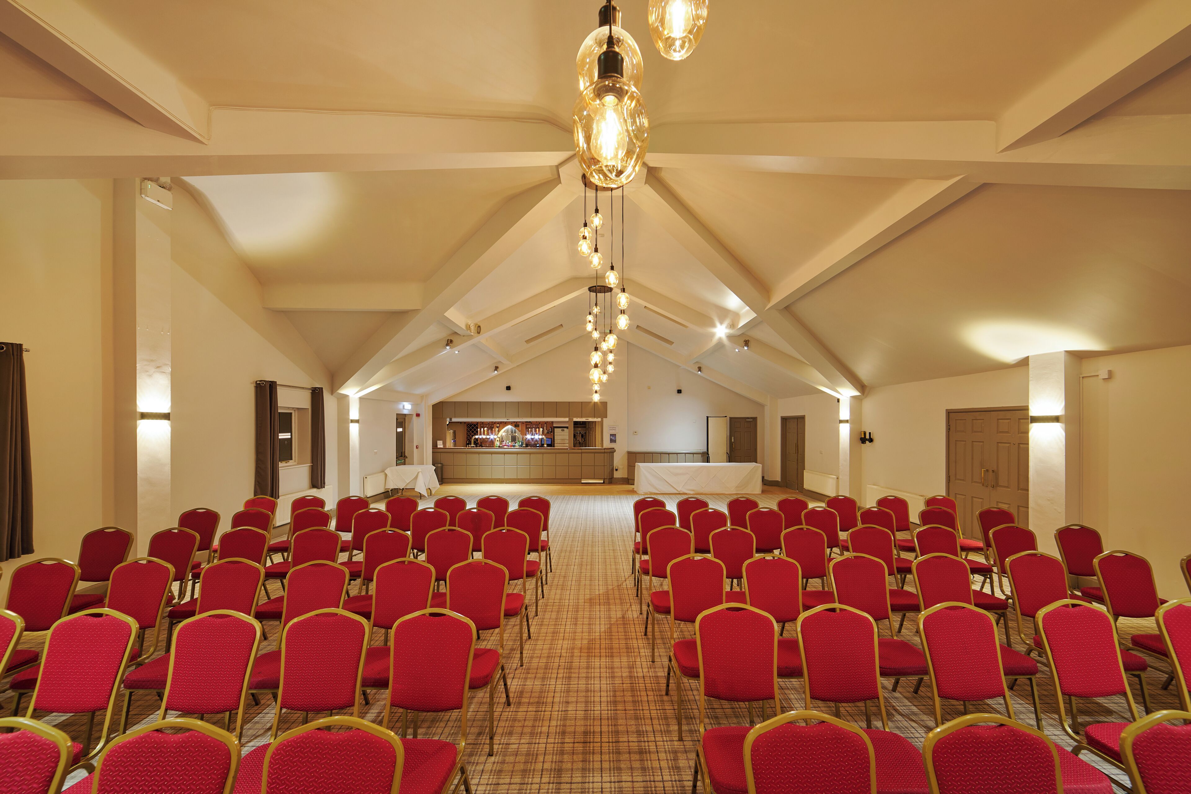 A conference room with rows of red chairs, a stage with a bar, and a high ceiling with hanging lights.