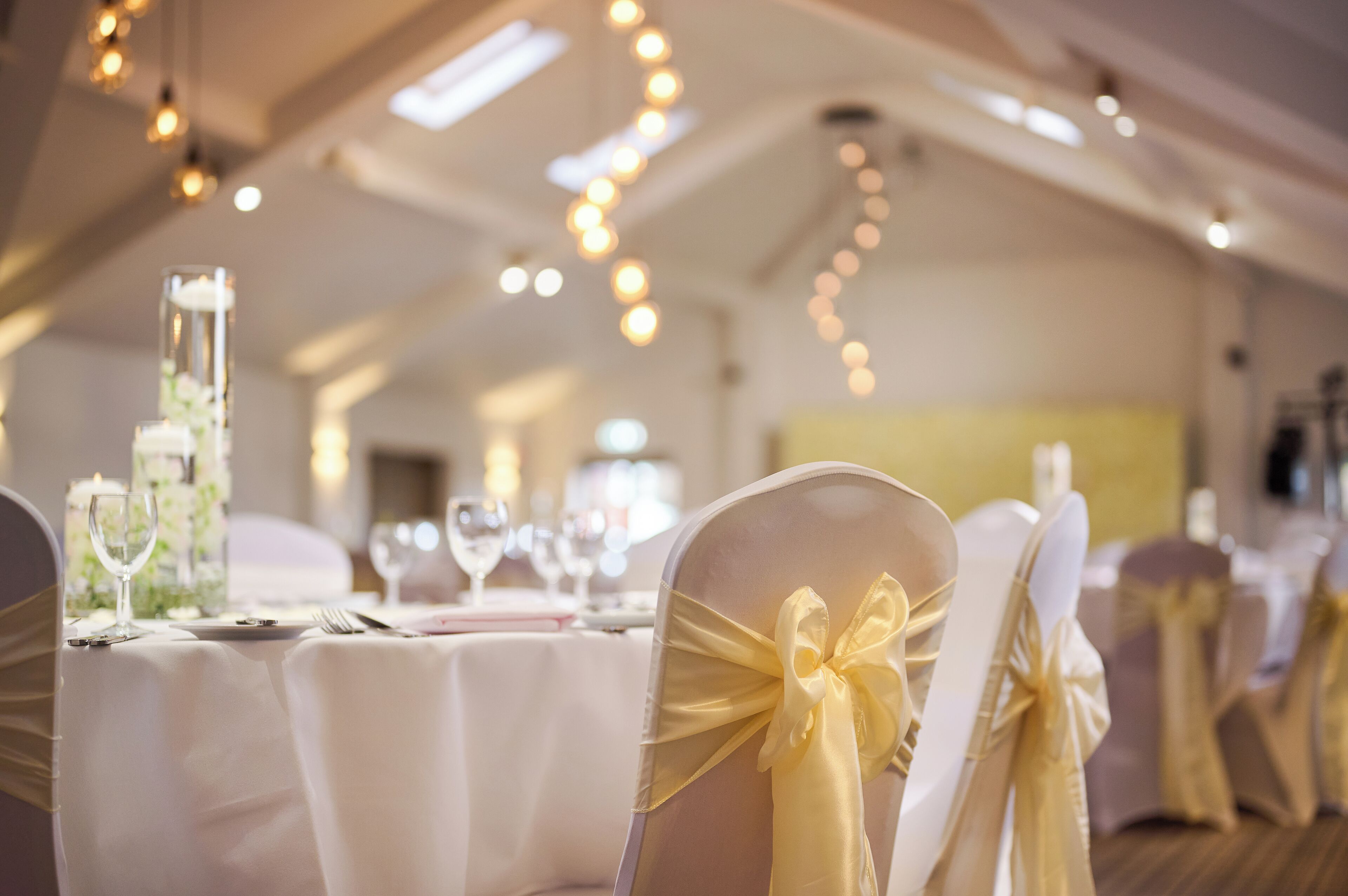 Una sala de banquetes amb taules preparades per a un esdeveniment formal, amb teles de taula blanques i cadirees amb galons daurats.