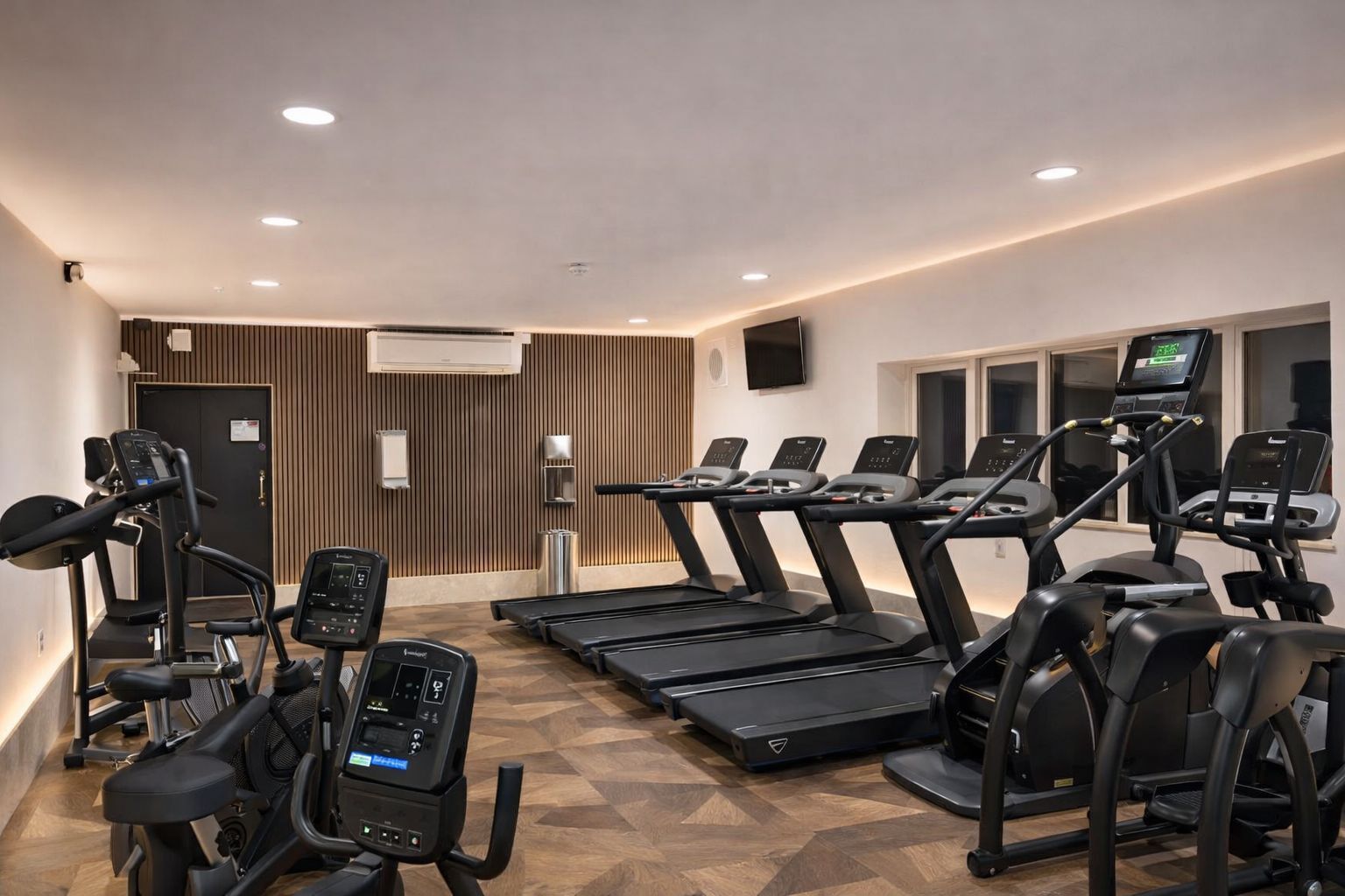 A gym with treadmills, elliptical machines, and a wall-mounted TV.