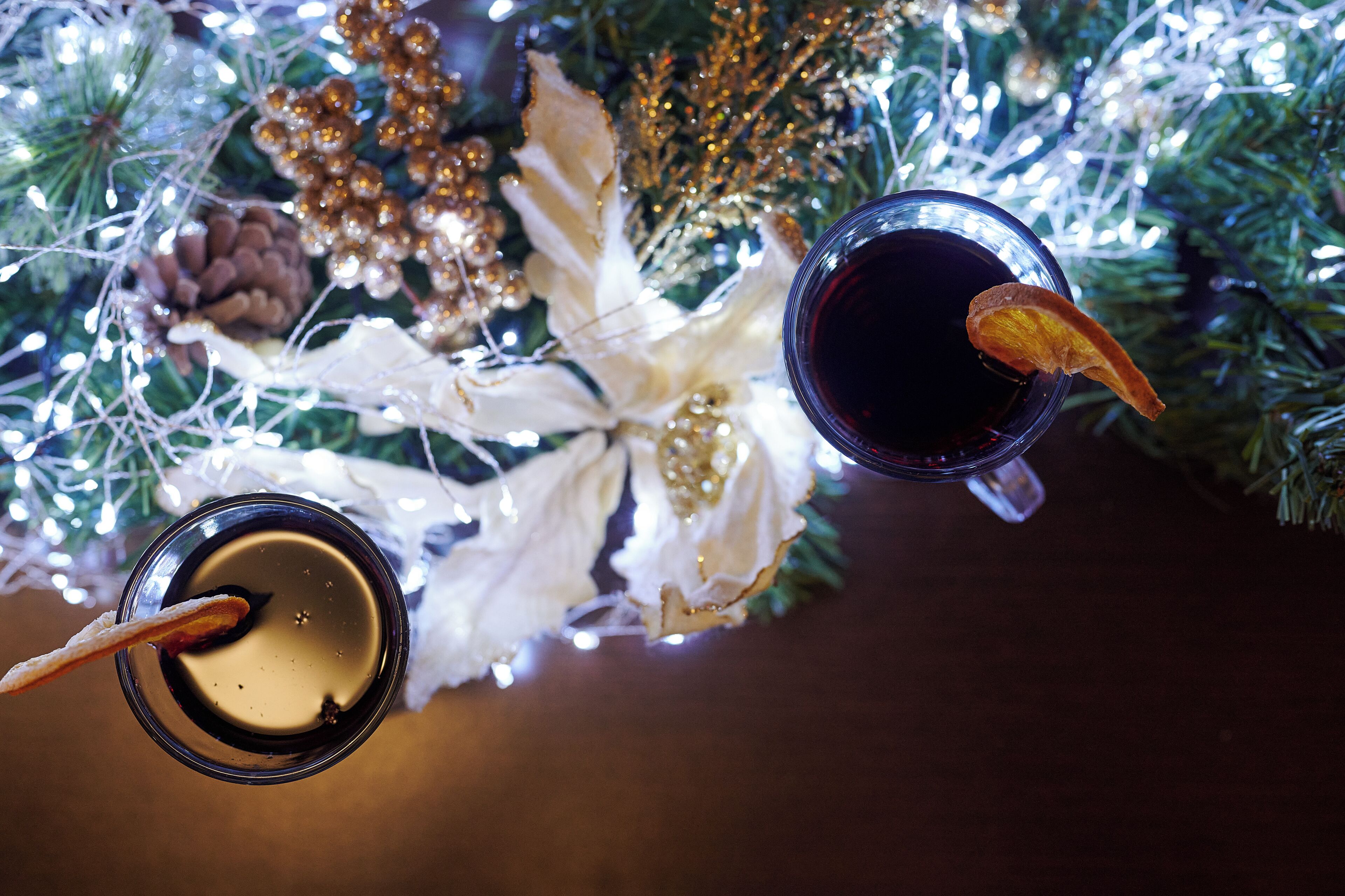 Dos vasos de líquido oscuro con adornos, sobre una superficie con un árbol de Navidad al fondo.