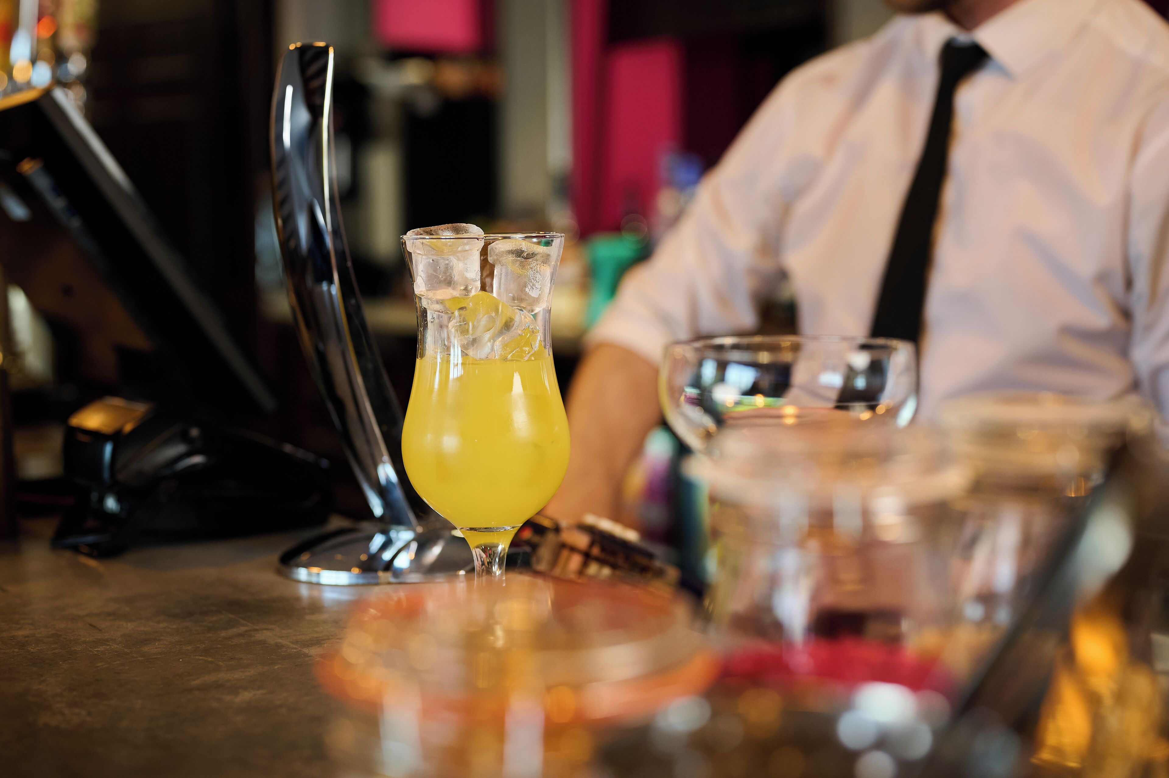 A bar setting with a glass pitcher of a yellow beverage, a metal shaker, and a glass.