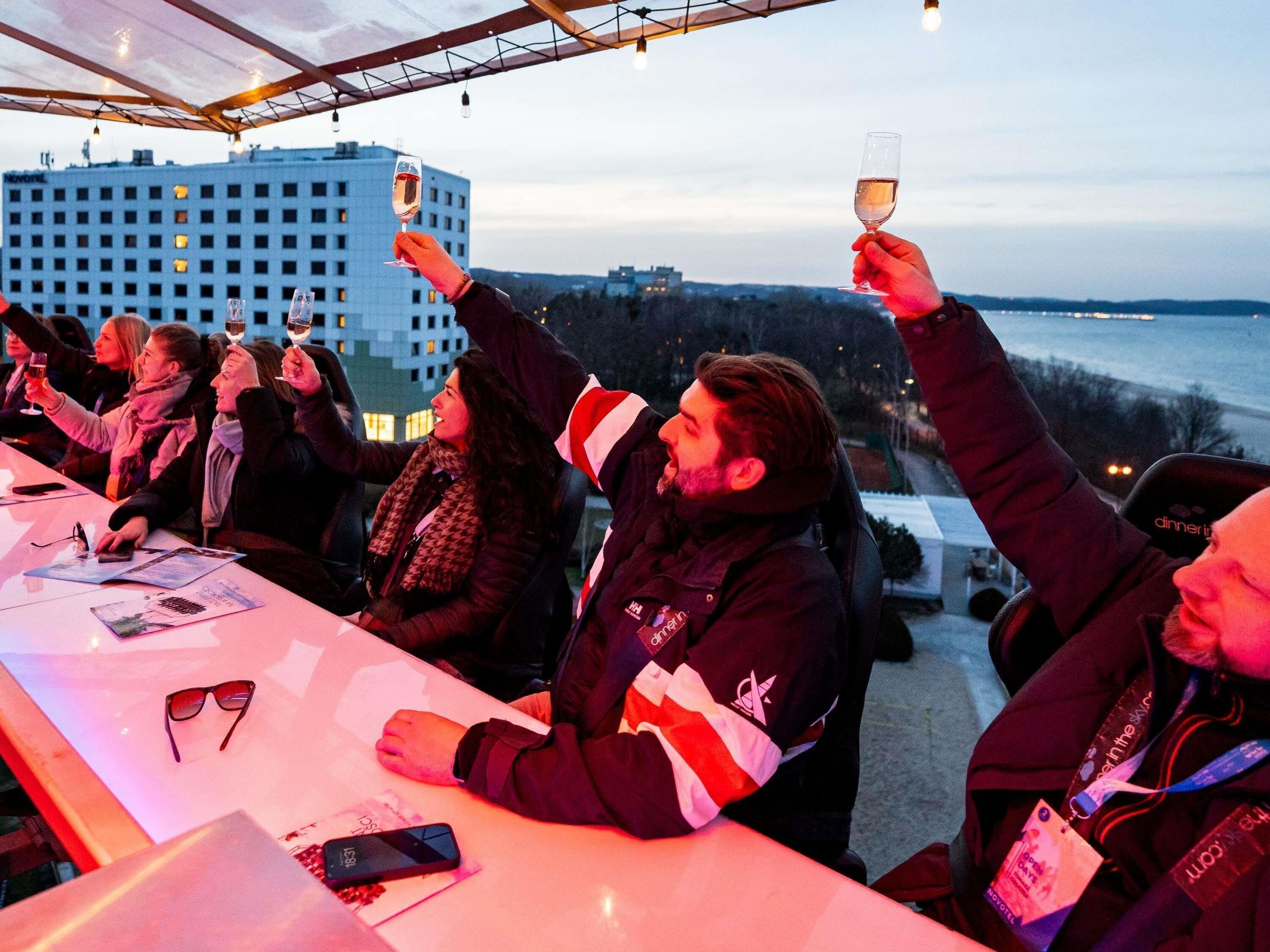 Un groupe de personnes lors d’un événement en plein air, tenant des verres, avec une vue sur la ville en arrière-plan.