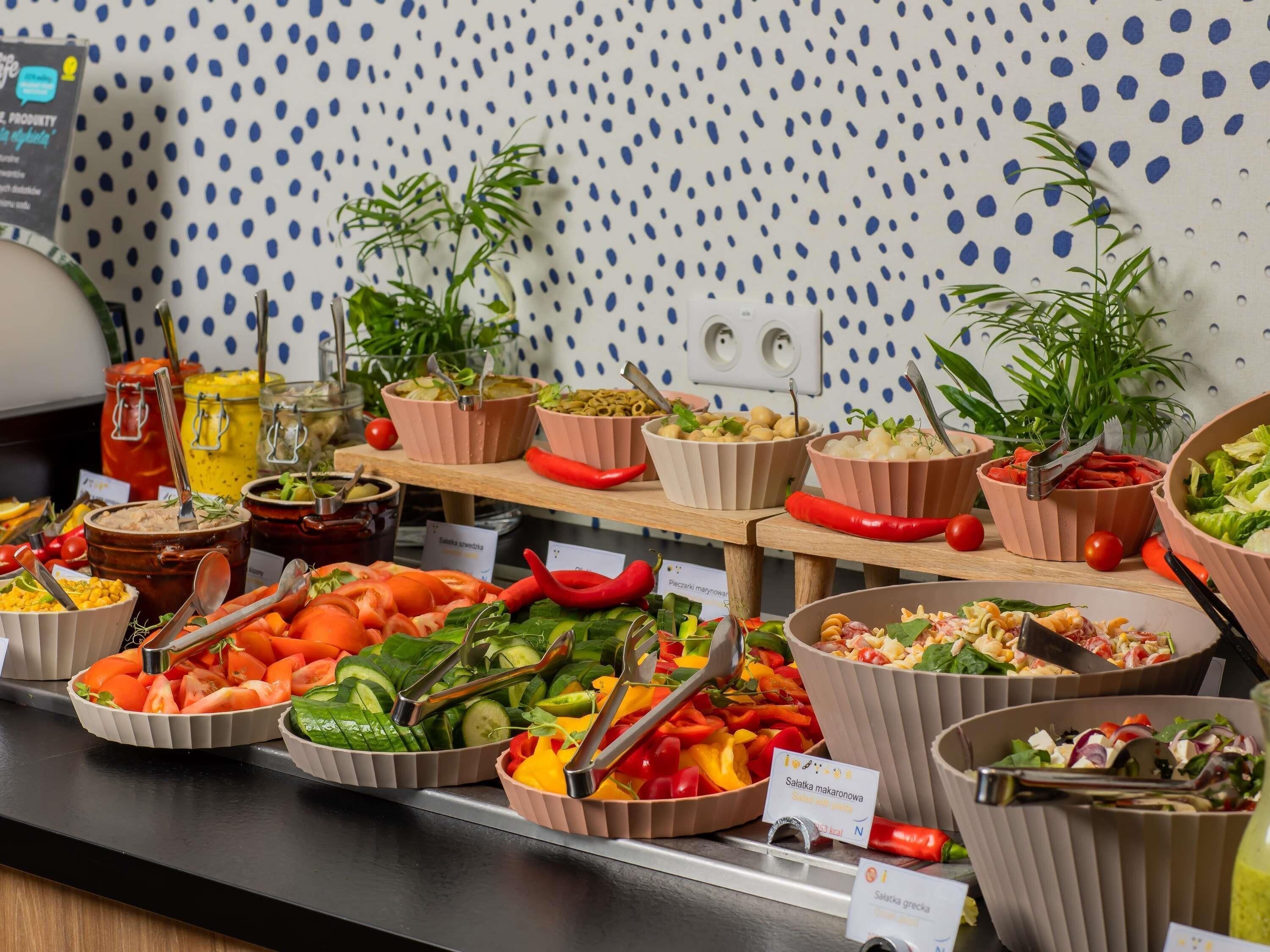 Un bufé con diversos platos, incluyendo ensaladas y verduras, dispuesto en un mostrador, con una pared de lunares al fondo.