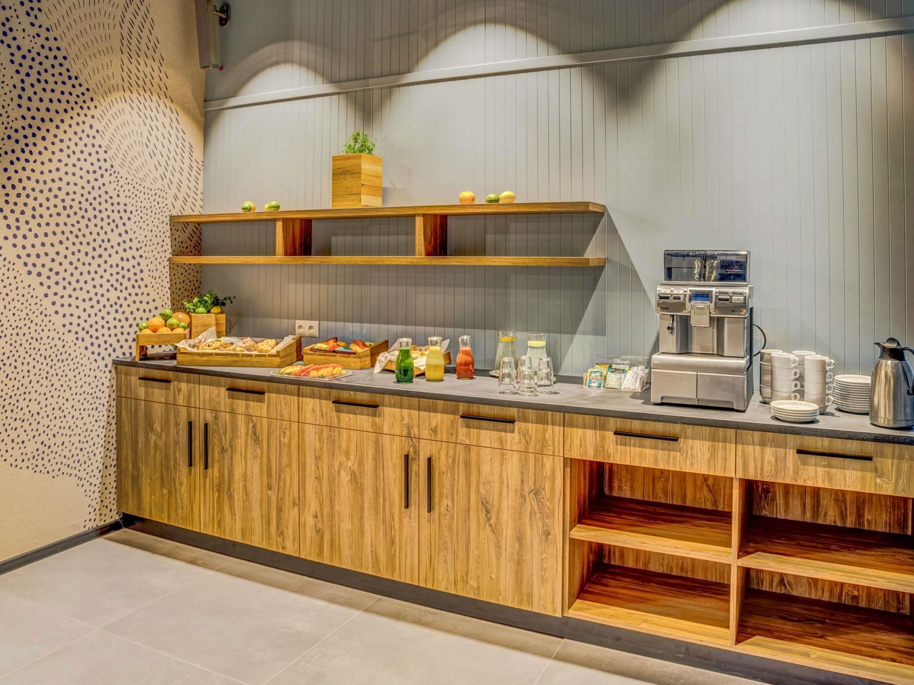 A modern kitchen with wooden cabinets, a coffee machine, and various food items on the counter.