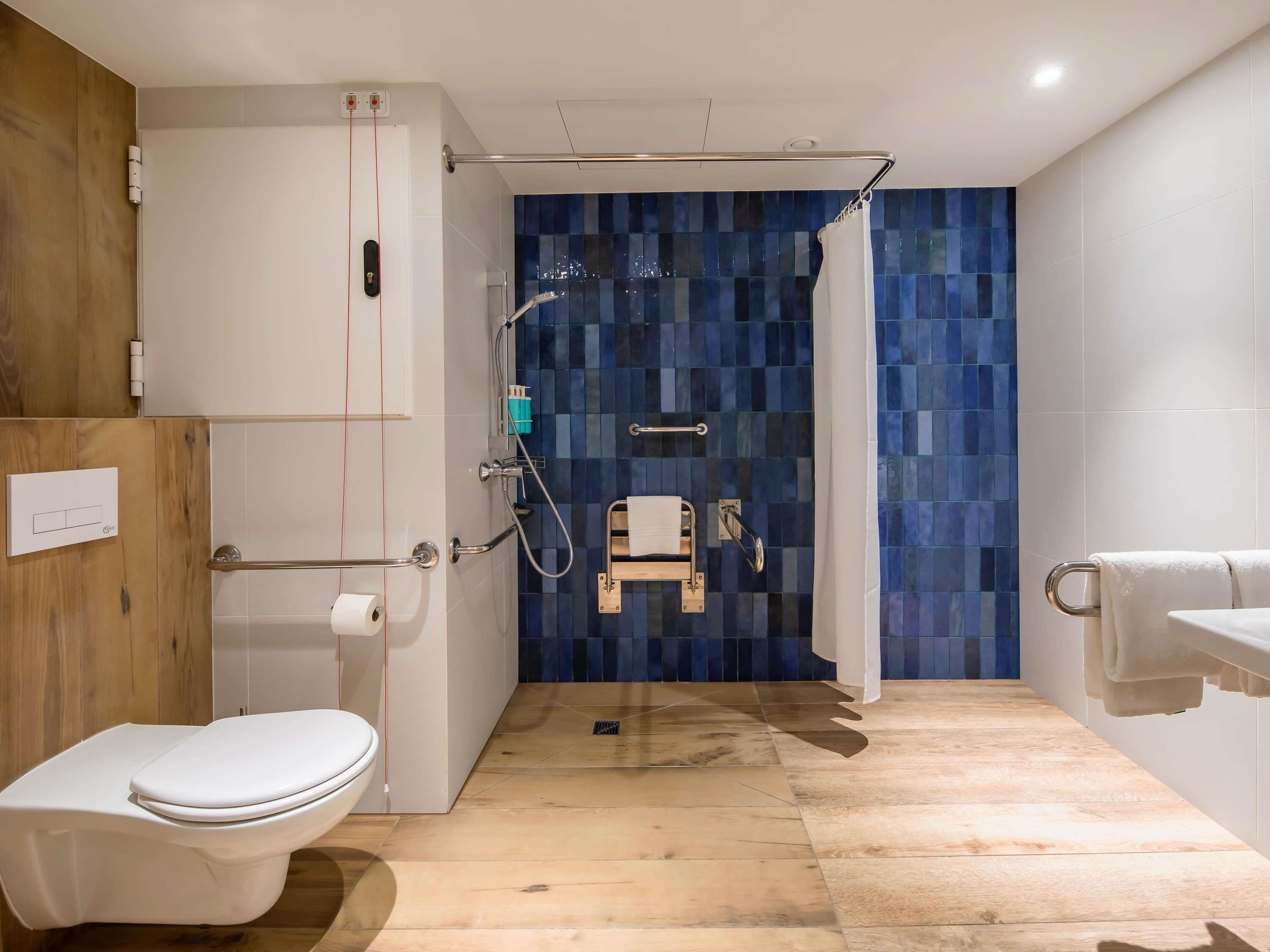 A modern bathroom with a white toilet, a shower area with a blue mosaic wall, and a wooden floor.
