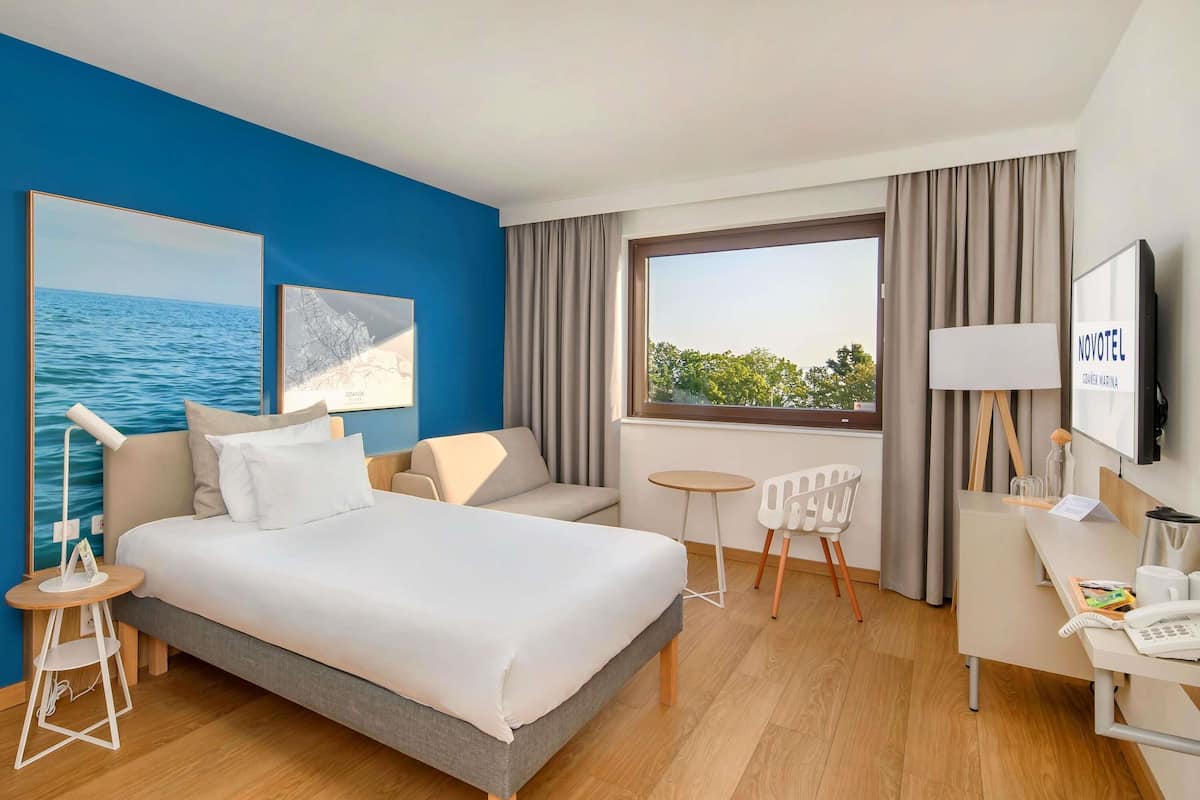 A hotel room with a bed, a desk, a chair, a TV, and a window with curtains.