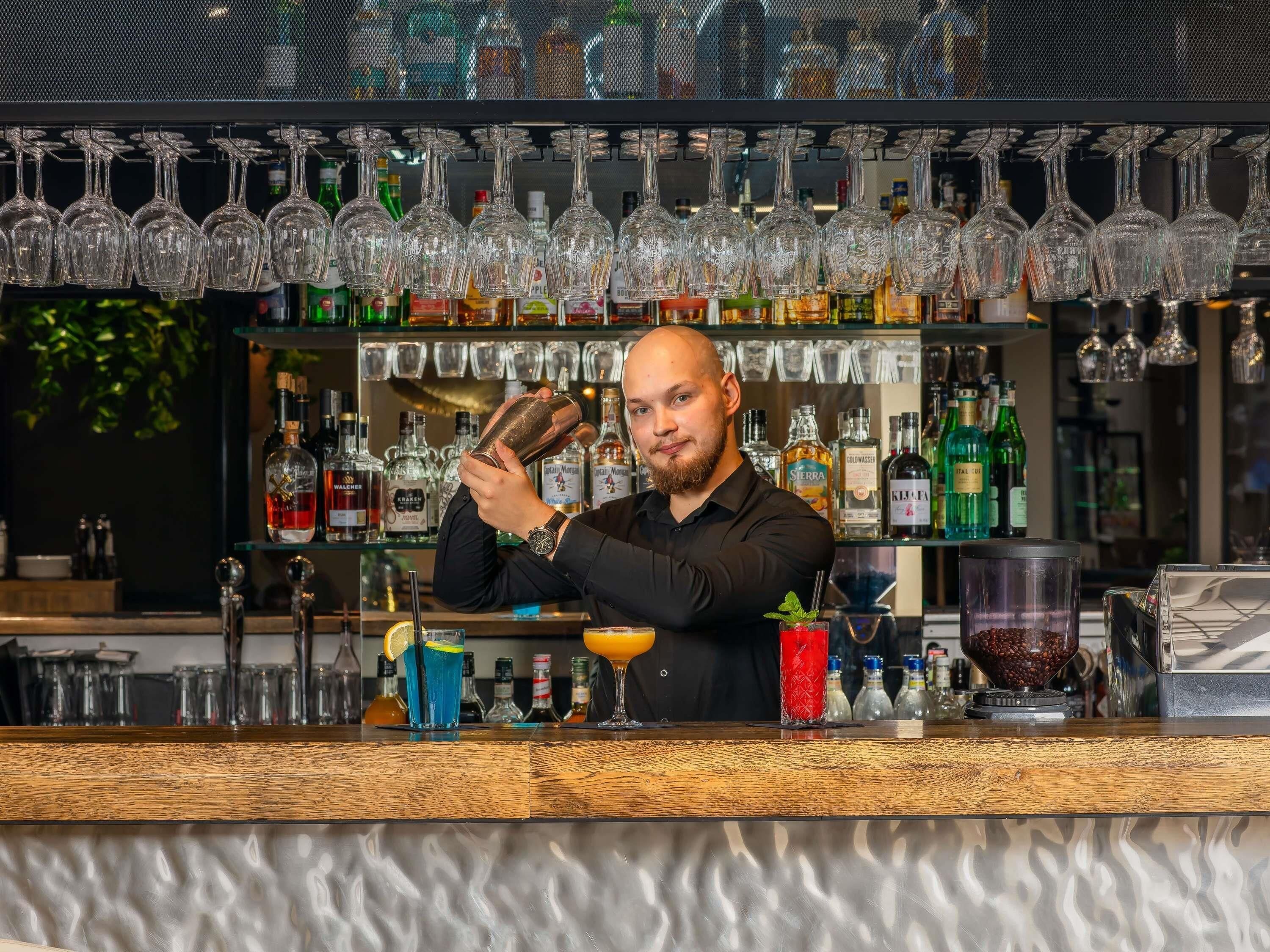 A bartender preparing a drink behind a bar with various bottles and glasses.
