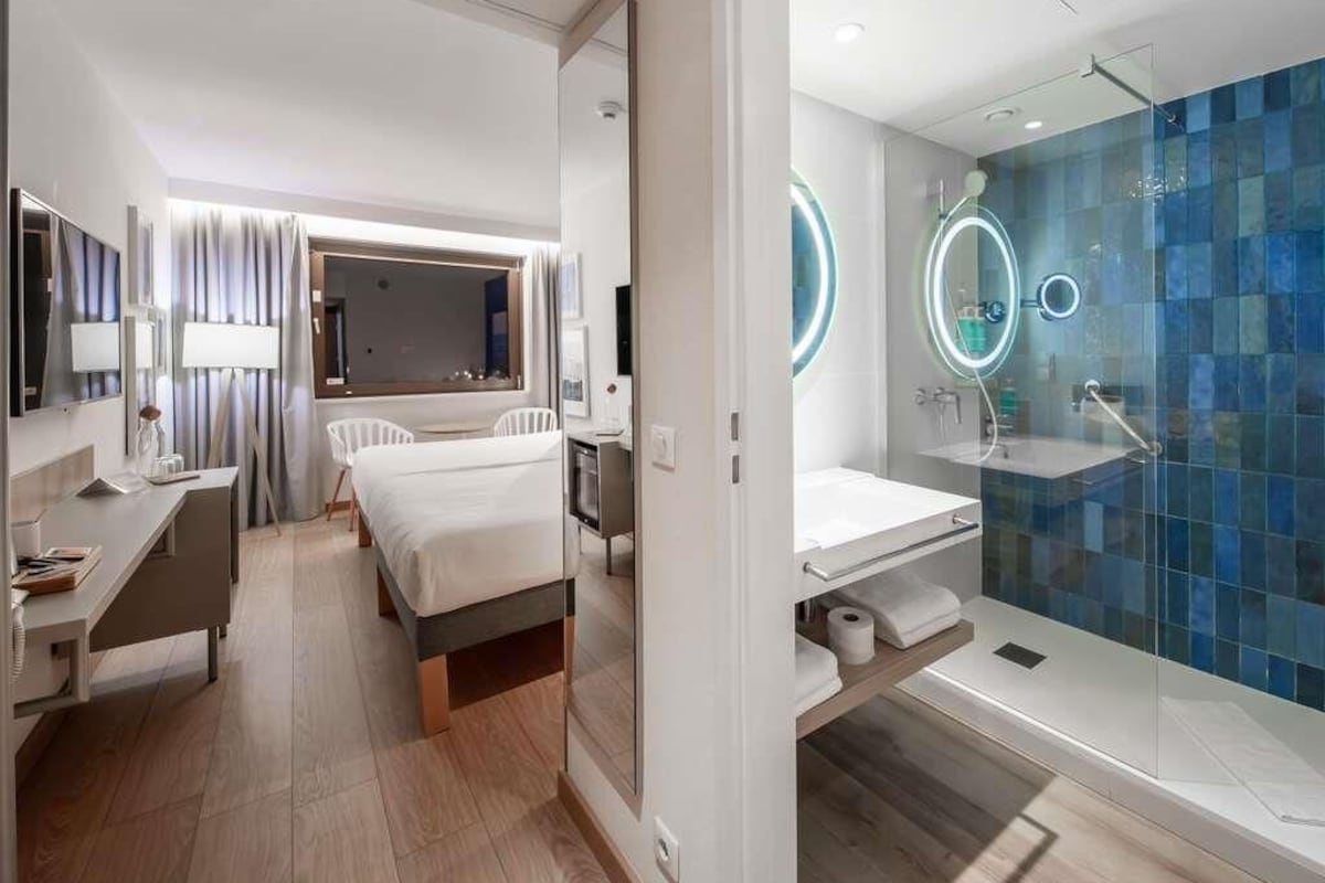 A modern hotel room with a bed, desk, and a bathroom with a glass shower enclosure.