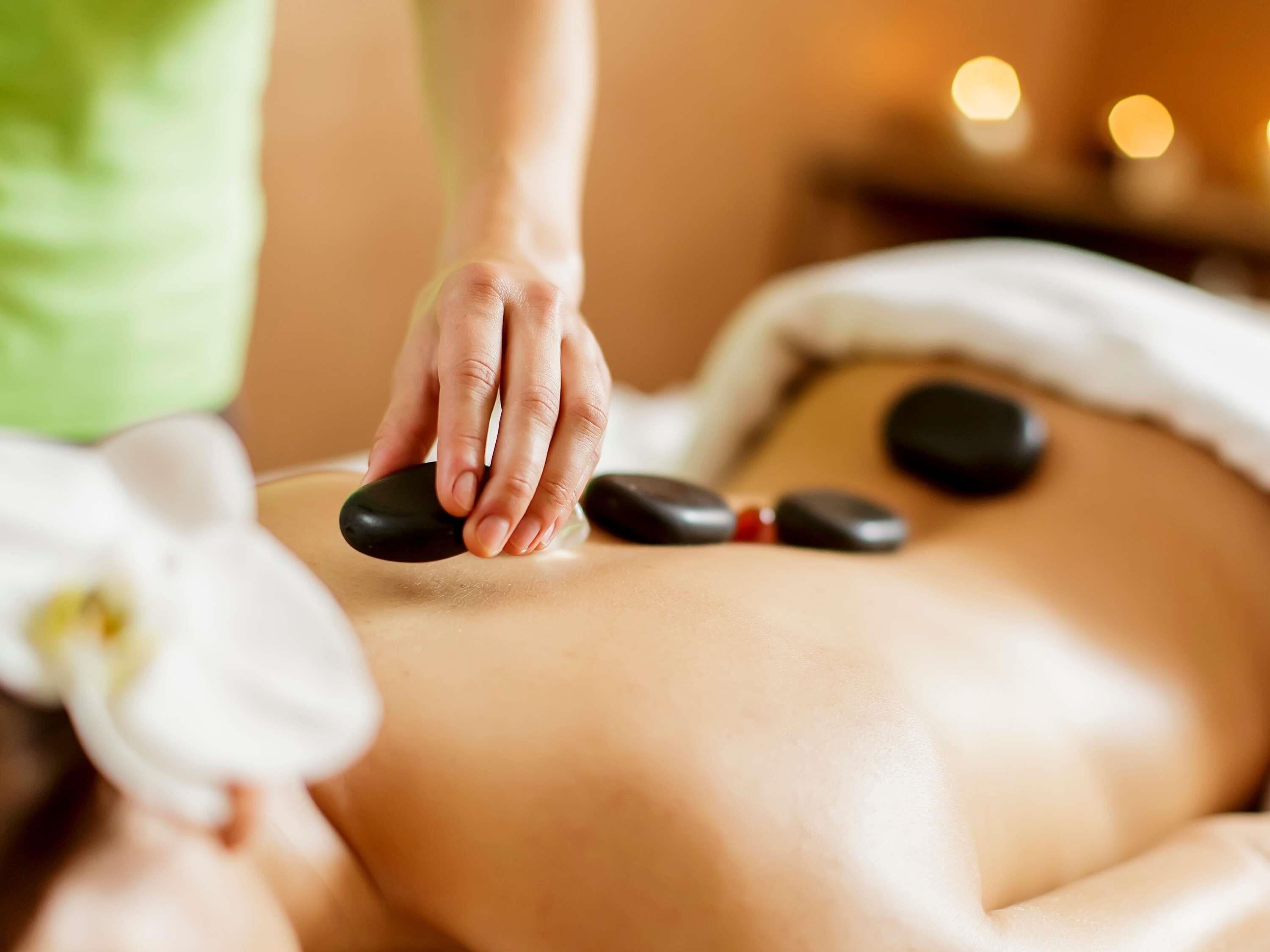 Een persoon ontvangt een steenmassage, er ligt een bloem op de tafel.
