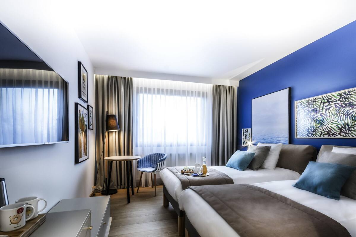 A hotel room with a bed, bedside table, chair, and a large window with curtains.