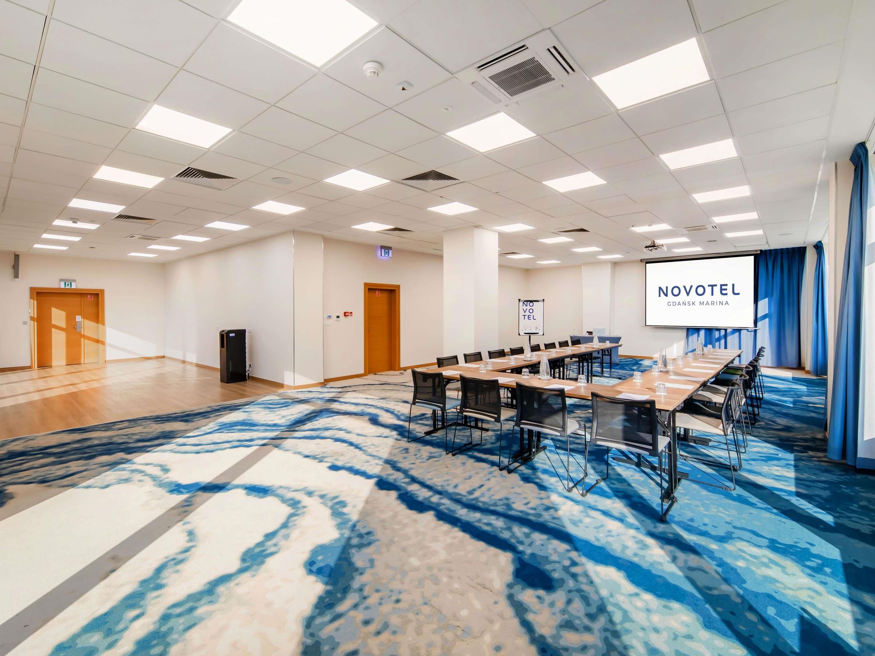 A conference room with a long table, chairs, a projector screen, and a carpeted floor.