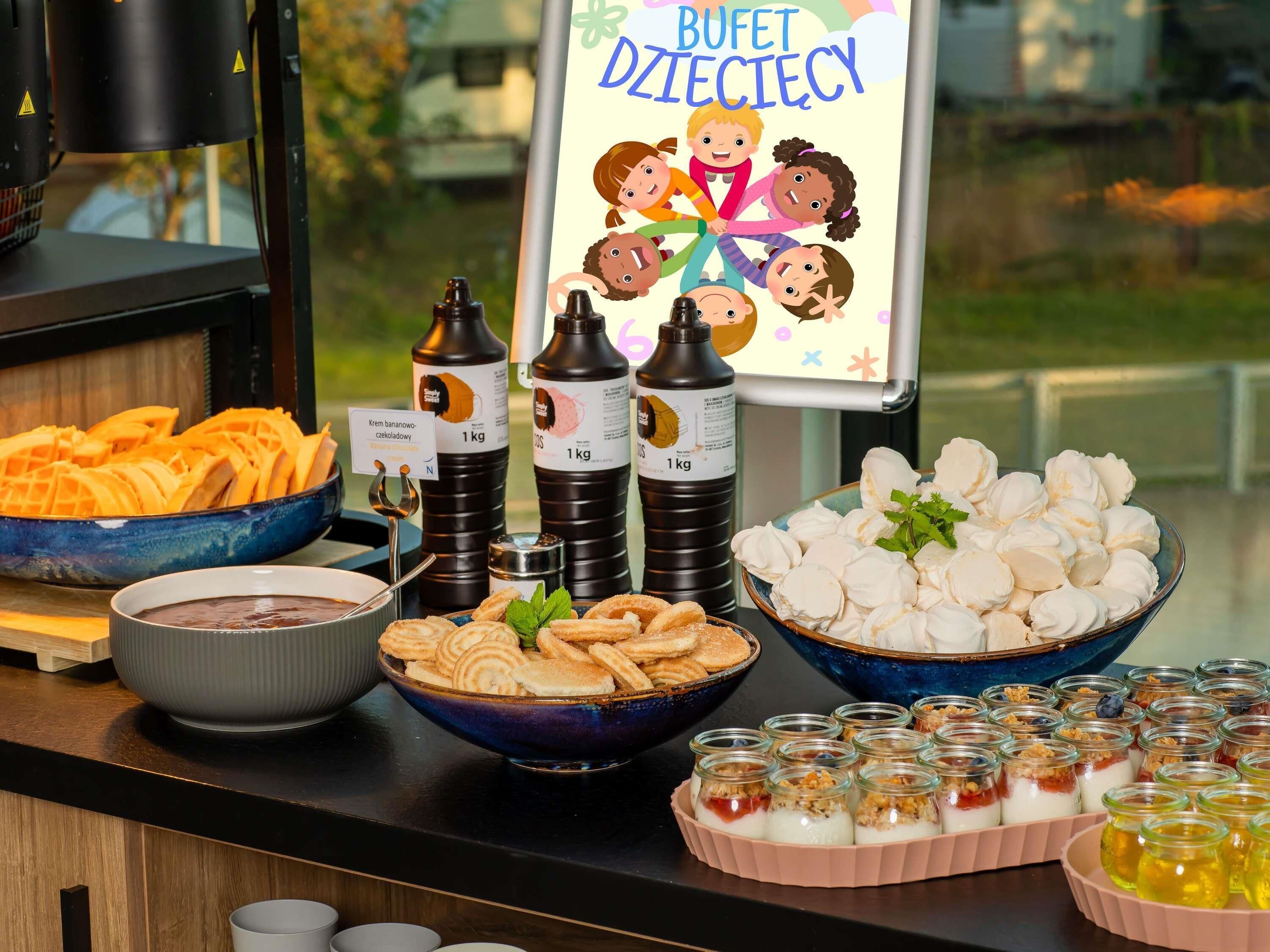 A buffet table with various food items, including waffles, pastries, and a sign reading 'BUFFET DZIECIĘCY'.
