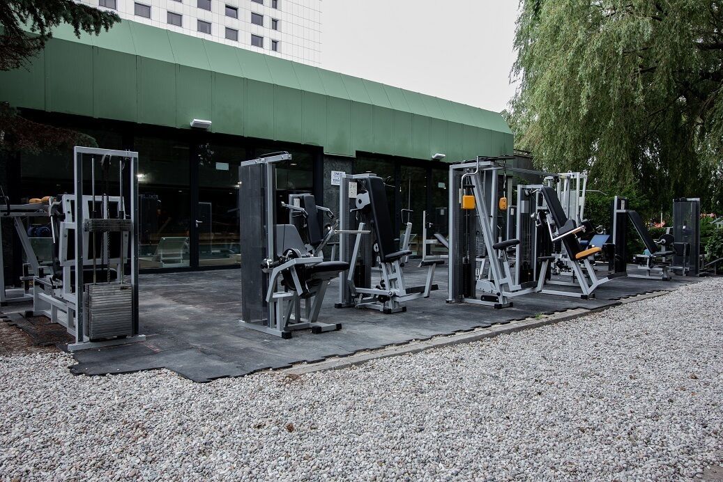 Un gimnasio con diferentes máquinas de ejercicio y un edificio verde al fondo.