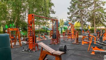 An outdoor gym with various exercise equipment, including benches and weightlifting stations.