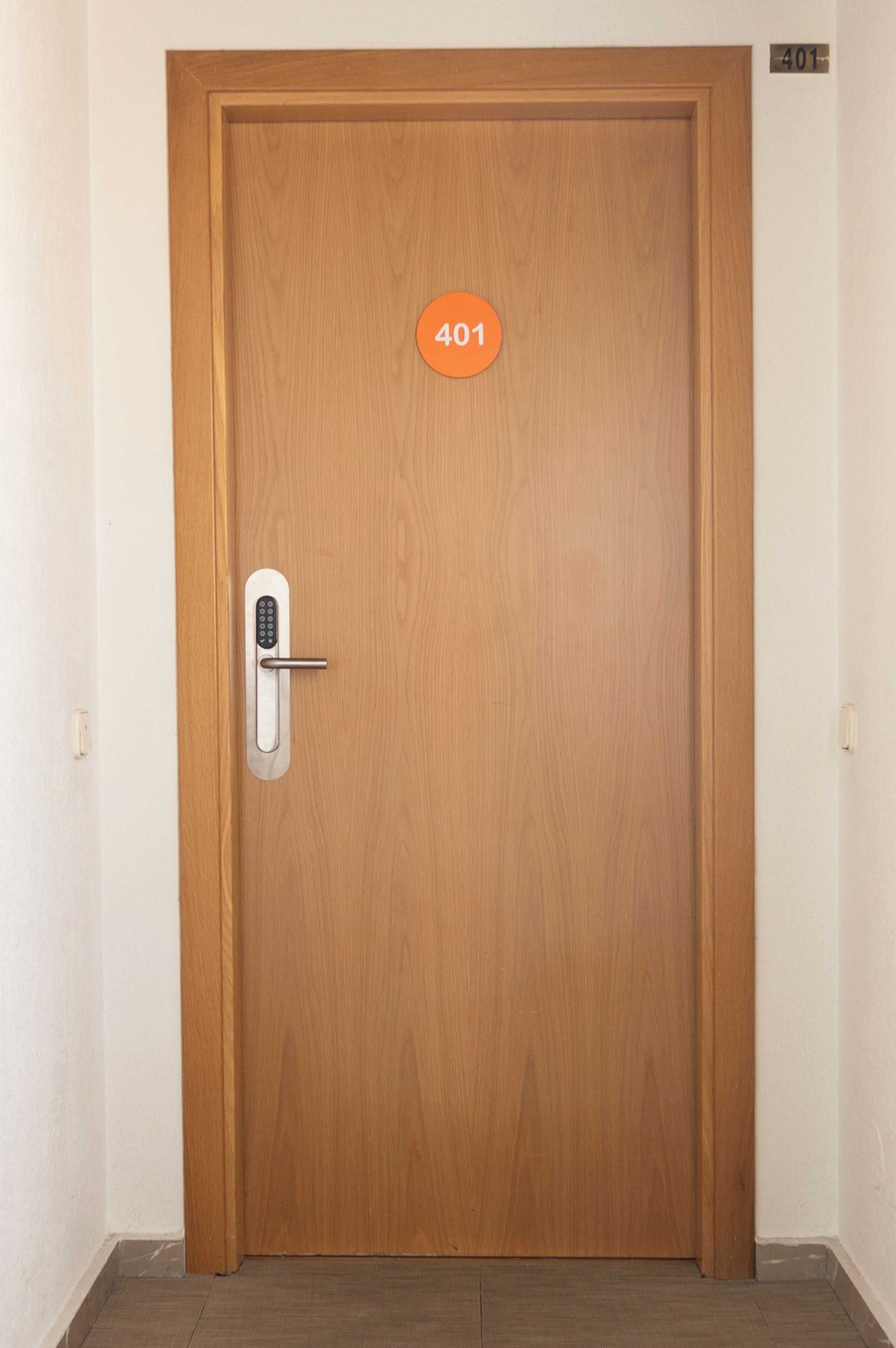 A wooden door with a numeric keypad lock, a small orange sign above it, and a number plate '401' on the wall to the right.