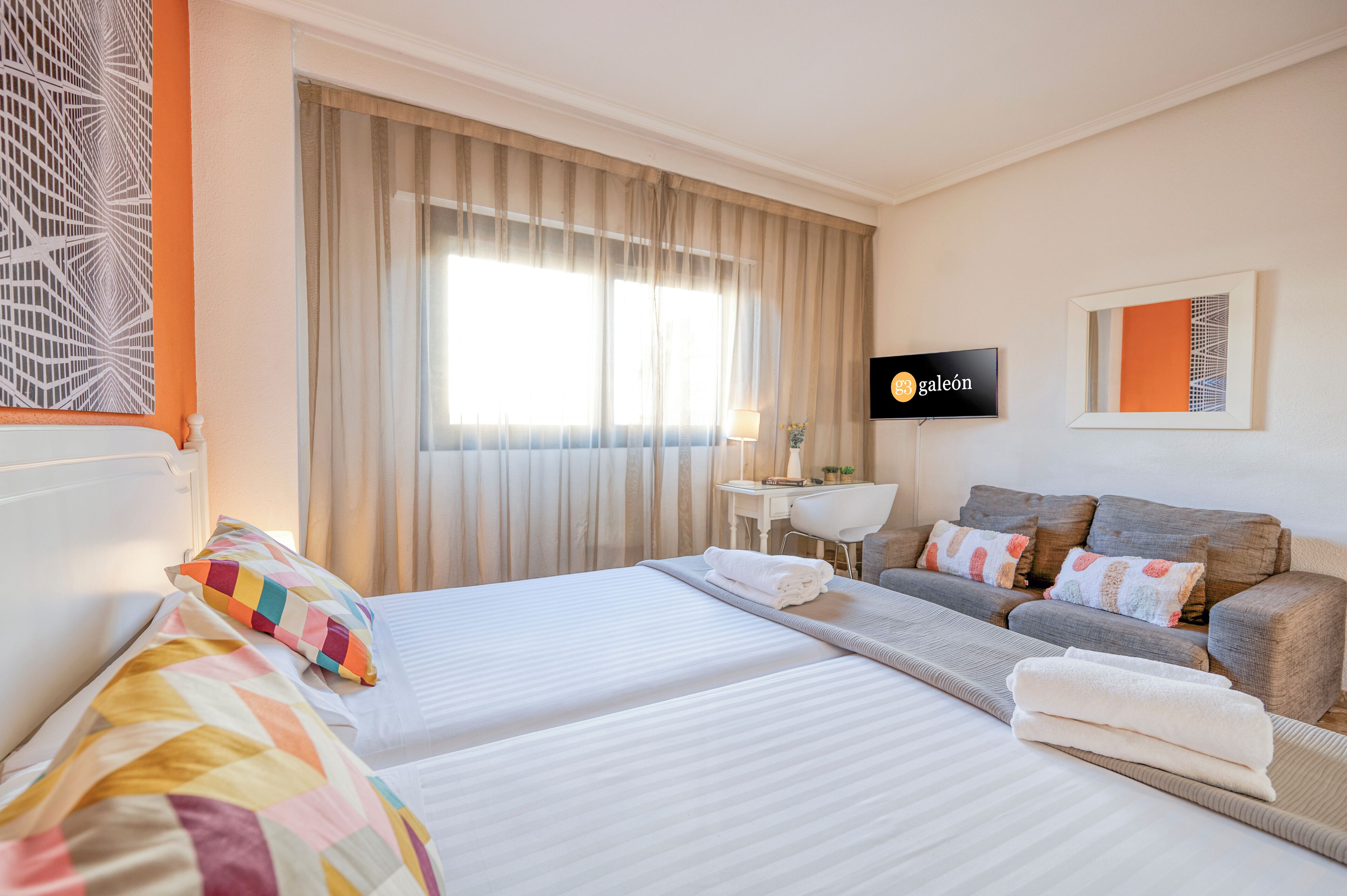 Une chambre d’hôtel avec deux lits, un canapé, une télévision et une fenêtre avec des rideaux.