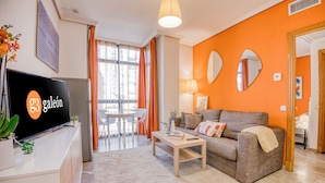 A modern living room with a sofa, coffee table, and TV. - Apartamentos G3 Galeón (Madrid)