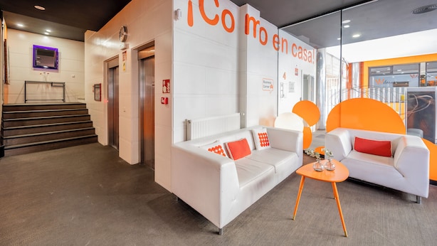 A modern lobby with white sofas, orange accents, and a visible elevator. - Apartamentos G3 Galeón (Madrid)