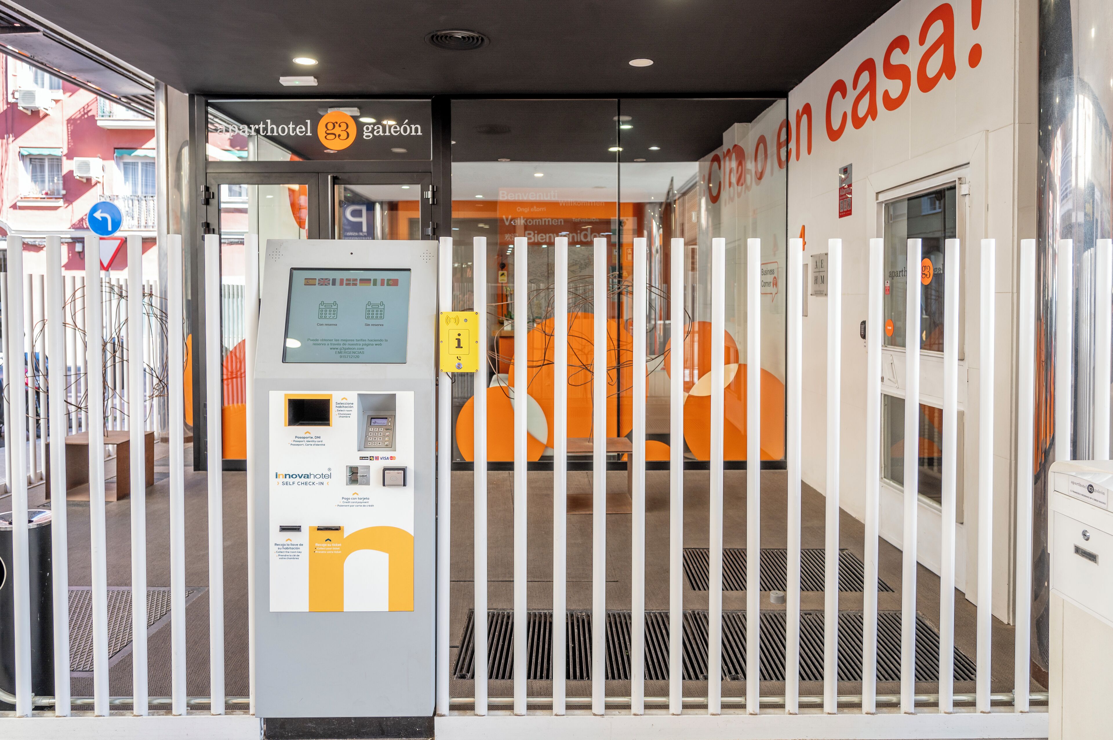 Entrada de hotel con quiosco de autoservicio, puertas de cristal y un letrero que dice 'G3 Gareón'.