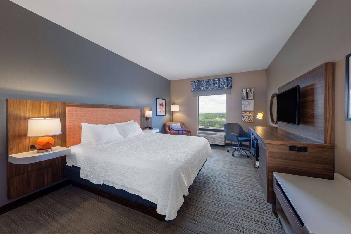 A hotel room with a bed, a desk, a chair, a TV, and a window with a view.
