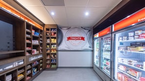 Innenansicht eines Supermarktes mit Regalen voller Snacks und Tiefkühlware, einer Wand mit der Aufschrift 'Treats' und einem Schild 'Willkommen in St. Robert' über dem Eingang.