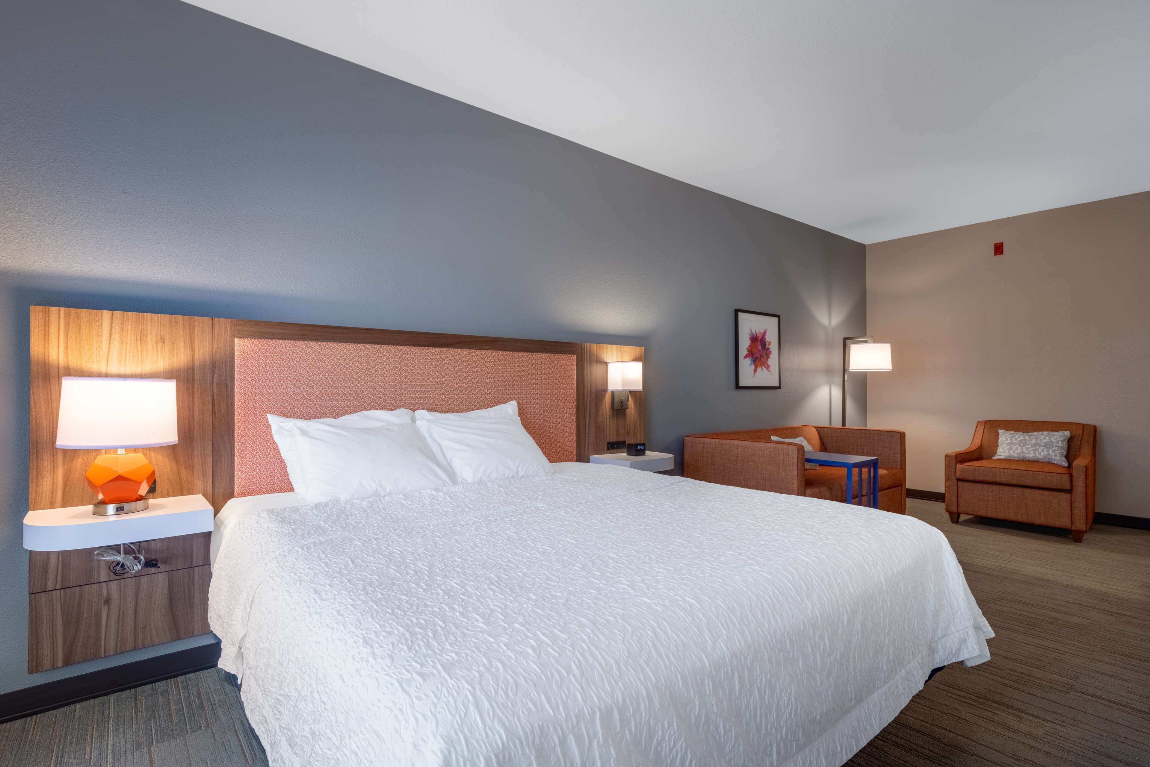 Une chambre d’hôtel avec un grand lit, une table de chevet avec une lampe, une chaise et une petite table.