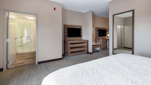 Ein Hotelzimmer mit einem großen Bett, einem an einer Holzeinrichtung montierten Fernseher, einem Spiegel und einer Tür zu einem Badezimmer.