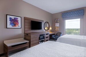 Una camera d'albergo con un letto, una scrivania con un computer, una televisione, un forno a microonde e un'ampia finestra con vista.