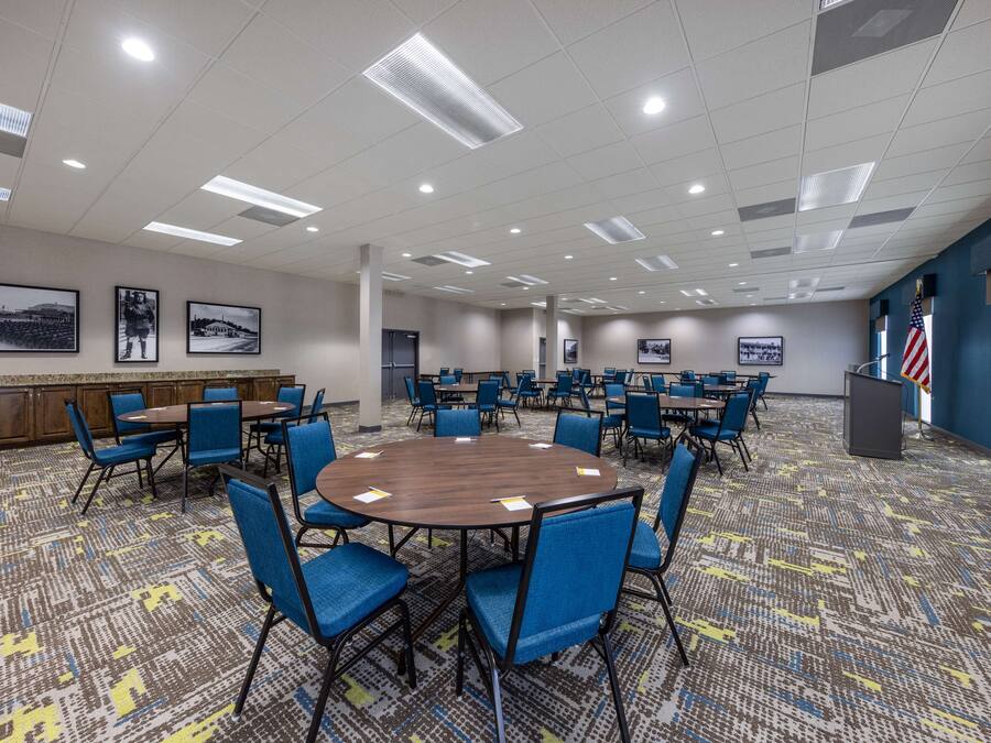 A conference room with a large round table surrounded by blue chairs, a patterned carpet, and framed pictures on the walls.