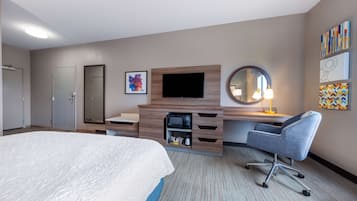 A hotel room with a bed, a desk with a chair, a television, a microwave, a mirror, and artwork on the walls.