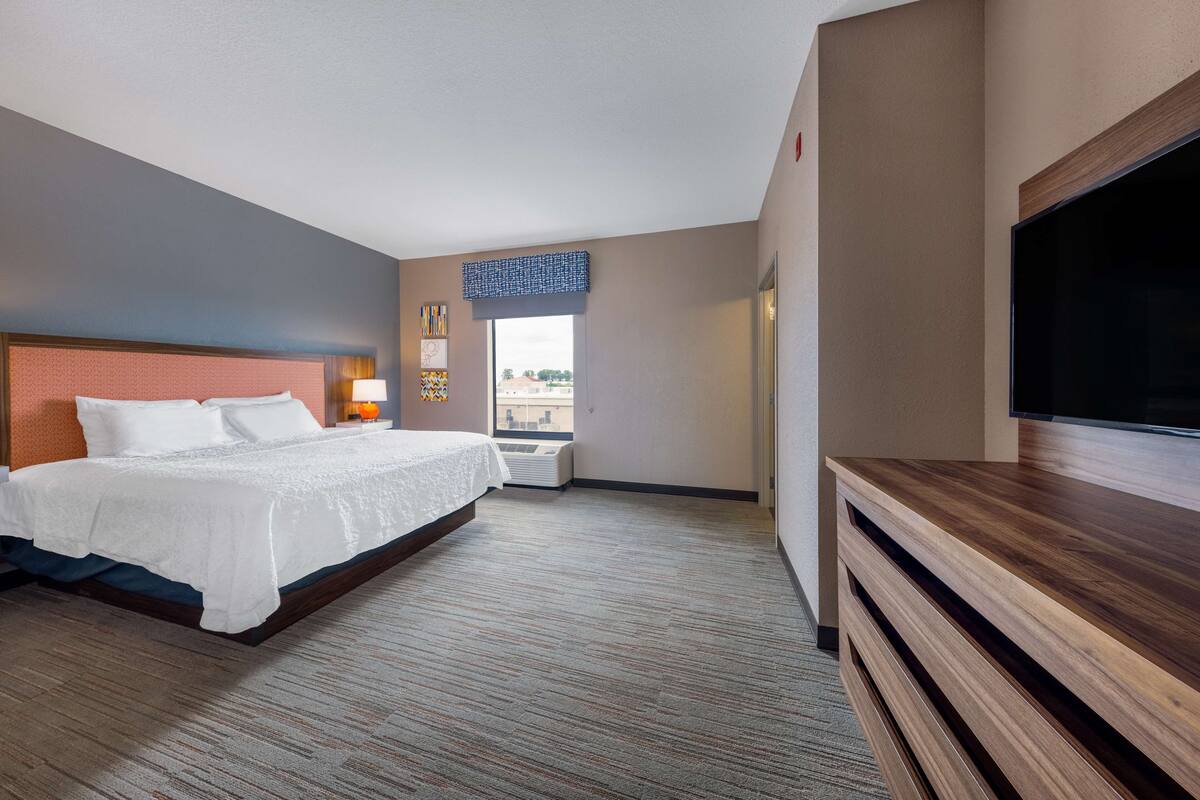 Quarto de hotel com uma cama grande, televisão de tela plana, janela com vista e televisão fixada na parede.
