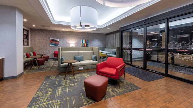 Eine moderne Lobby mit einer Couch, einem roten Sessel und einem Couchtisch. Ein großes Fenster bietet Blick auf die Stadt.
