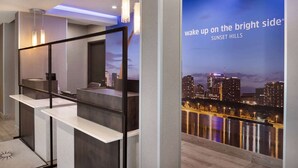 A modern hotel lobby with a cityscape view, a reception desk, and ambient lighting. - La Quinta Inn & Suites by Wyndham St Louis Route 66 (St. Louis)