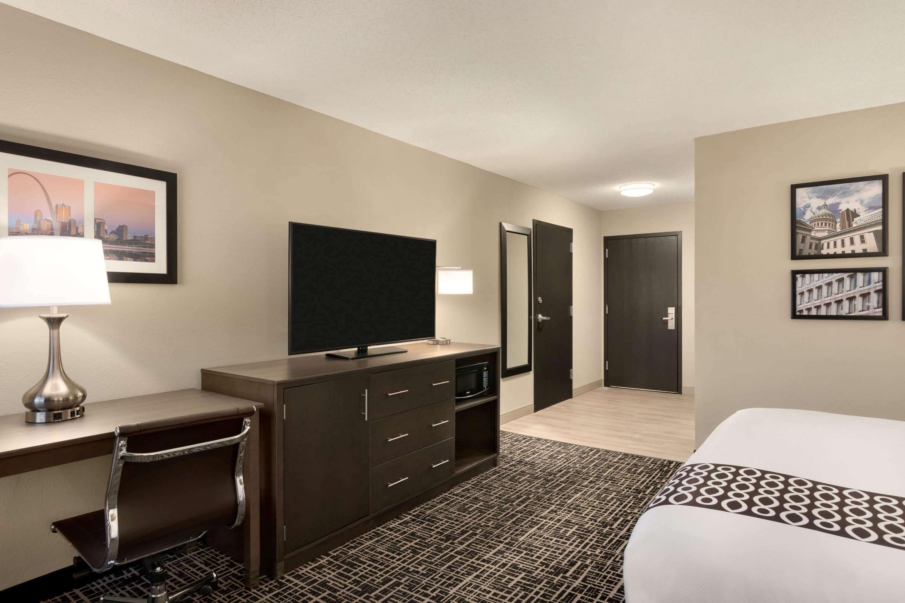A hotel room with a bed, desk, chair, television, and a door leading to another room.