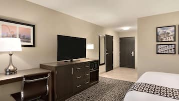 A hotel room with a bed, desk, chair, television, and a door leading to another room.