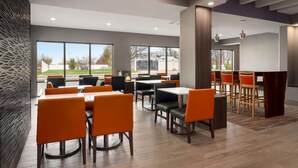 A modern dining area with multiple tables and chairs, large windows offering a view of the outdoors, and a mix of natural and artificial lighting. - La Quinta Inn & Suites by Wyndham St Louis Route 66 (St. Louis)