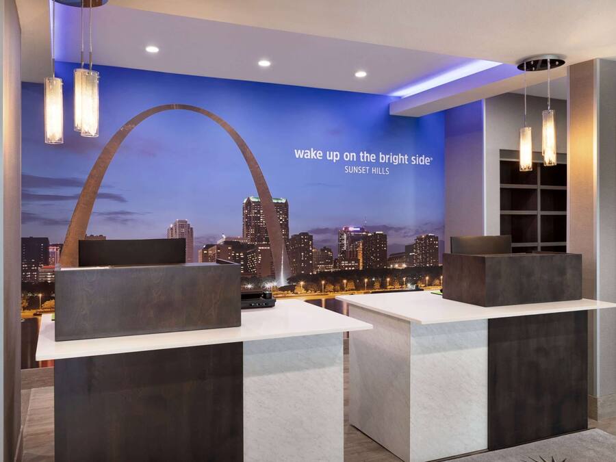 Een moderne hotel lobby met een stadsgezicht muurschildering, een receptiebalie en moderne verlichtingsarmaturen.