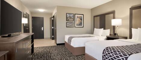 A hotel room with two beds, a desk with a flat-screen TV, a dresser, and a patterned carpet.