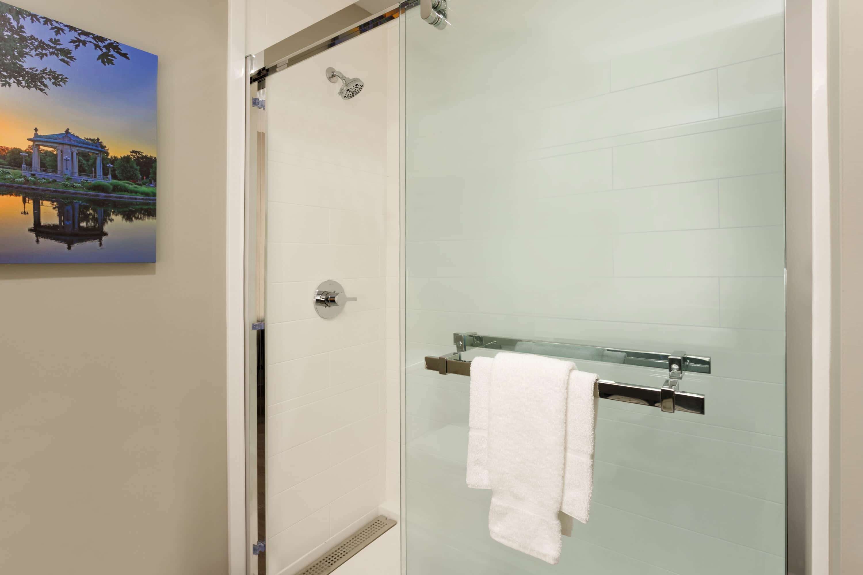 A glass-enclosed shower with a glass door, a towel rack with a white towel, and a painting of a building on the wall.