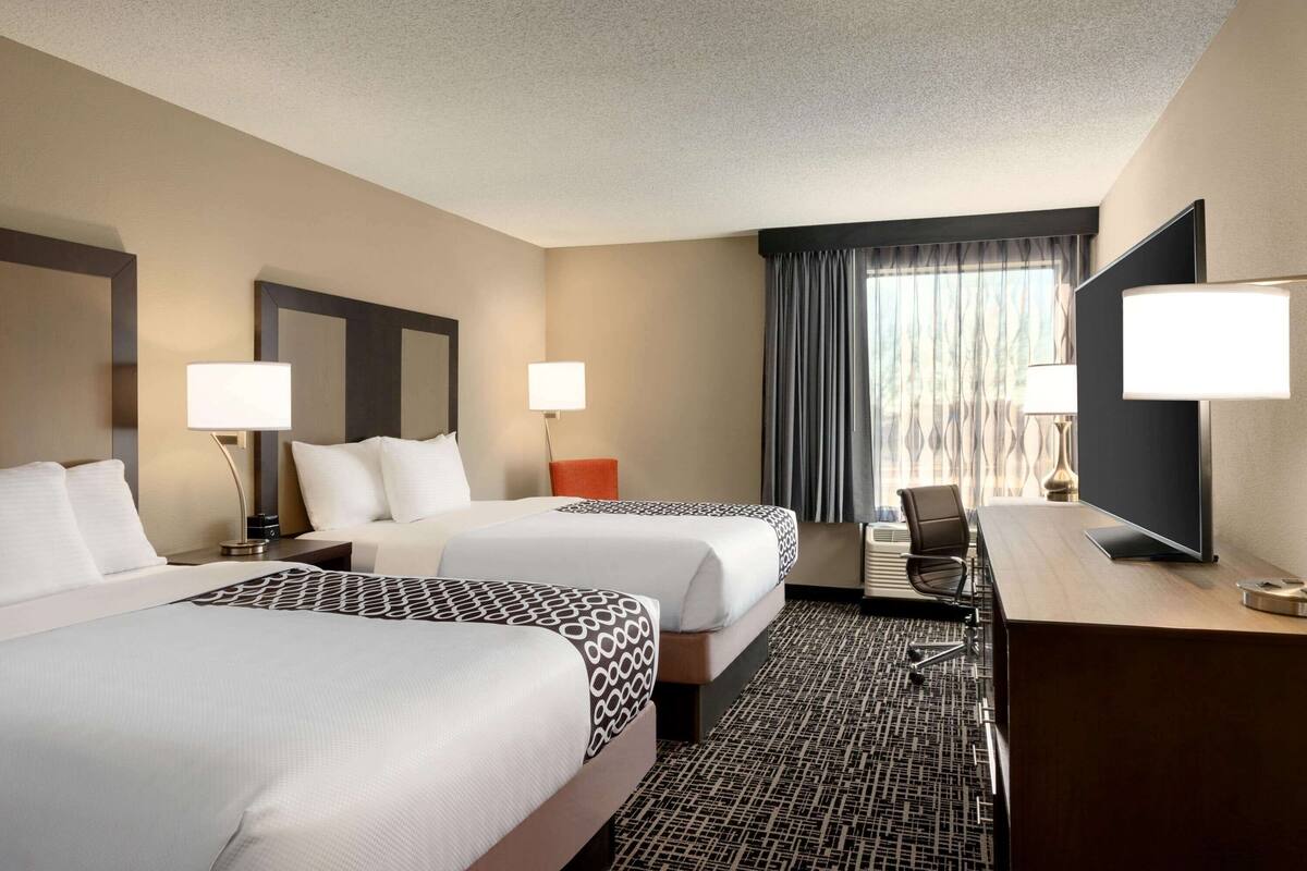 Une chambre d’hôtel avec deux lits, un bureau, une télévision et une grande fenêtre avec des rideaux.