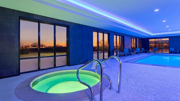 A swimming pool with a metal ladder, surrounded by chairs and large windows offering a view of the sunset. - La Quinta Inn & Suites by Wyndham St Louis Route 66 (St. Louis)