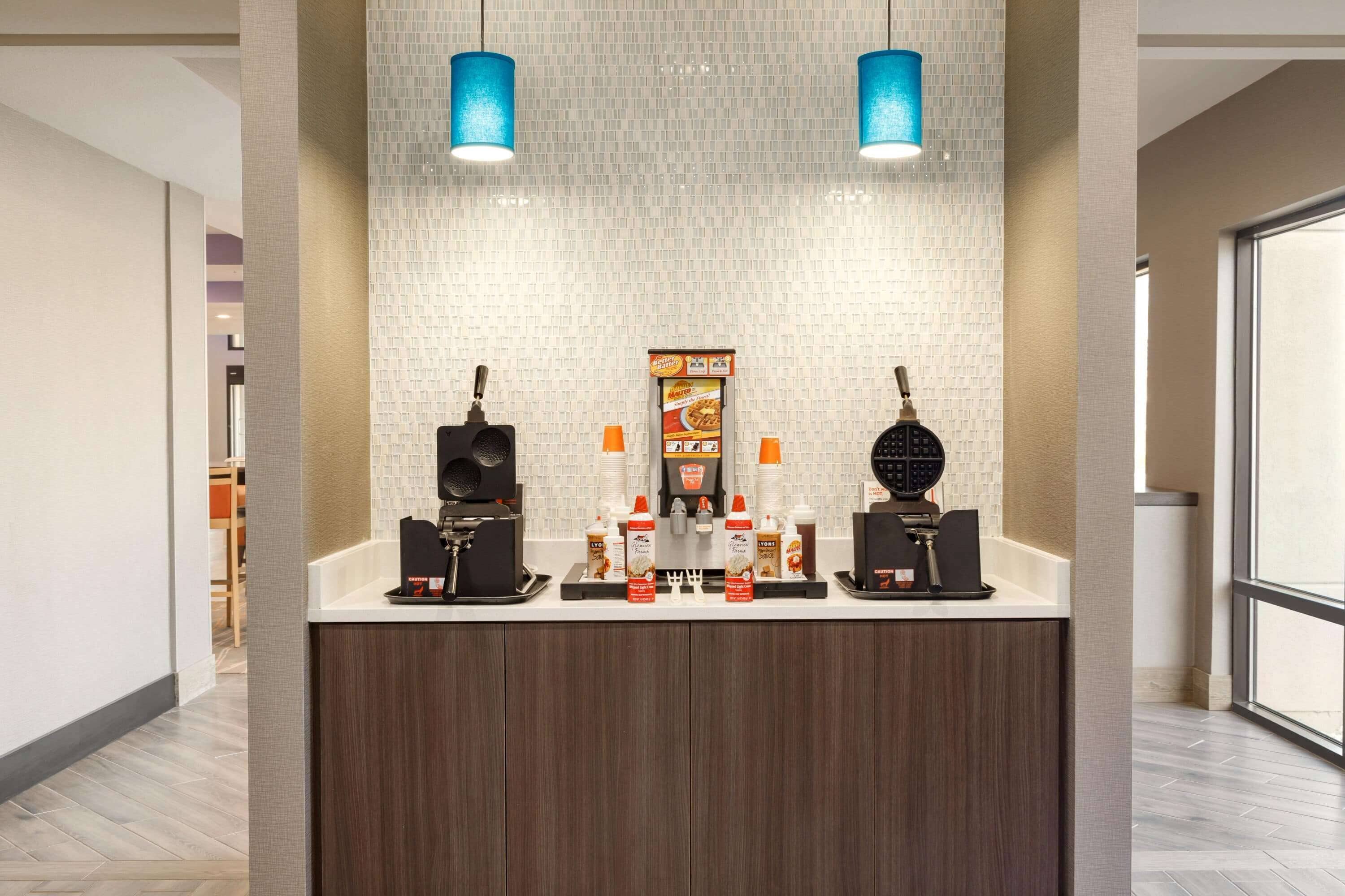 Una estación de café moderna con dos máquinas de espresso, una variedad de cápsulas de café y una pizarra con el menú.