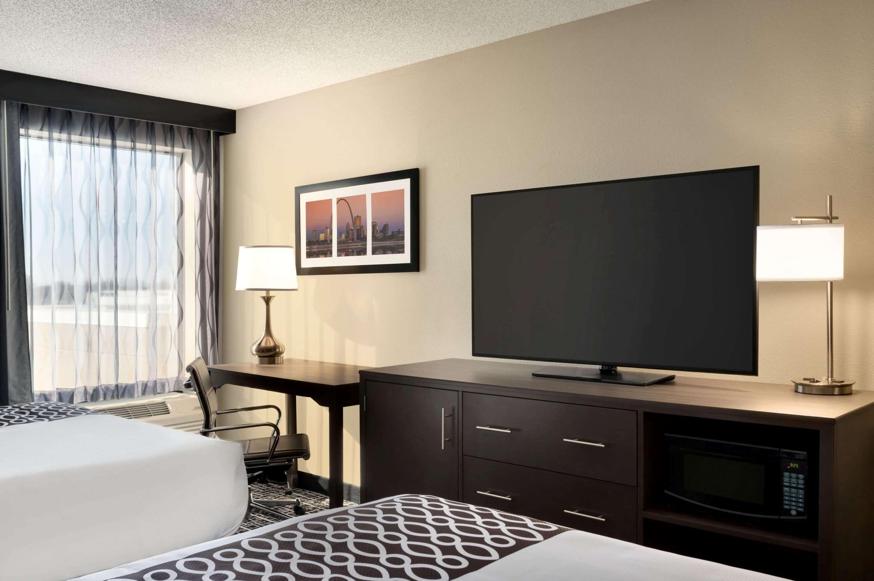 A hotel room with a bed, a desk, a television, a lamp, and a framed picture on the wall.
