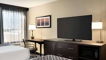 A hotel room with a bed, a desk, a television, a lamp, and a framed picture on the wall.