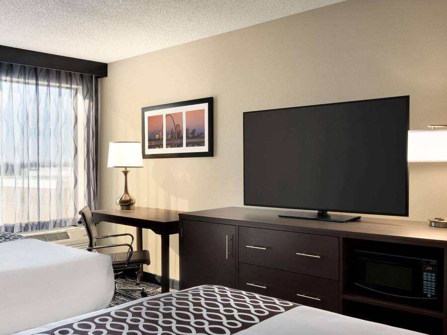A hotel room with a bed, a desk, a television, a lamp, and a framed picture on the wall.